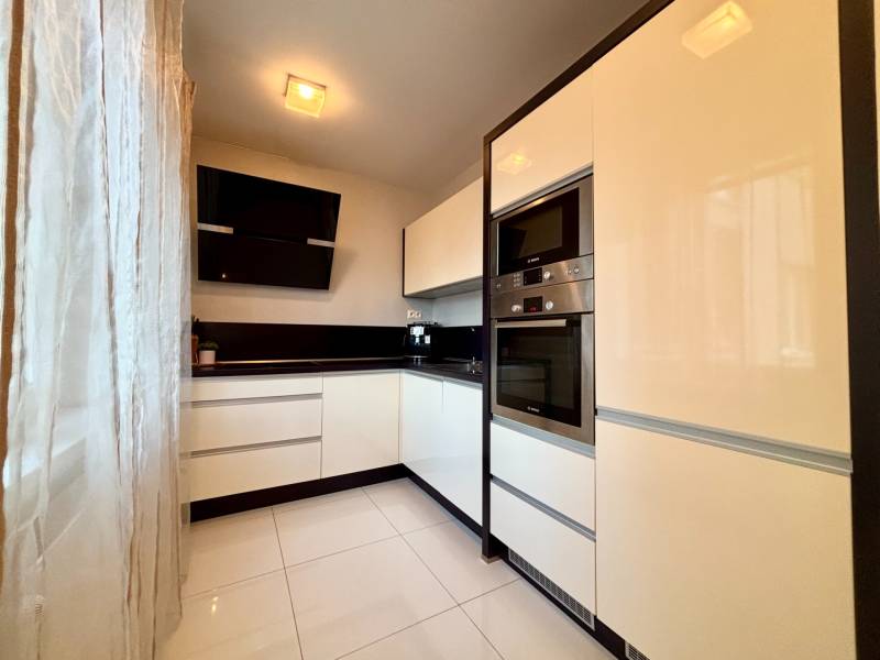 Fehér konyha fekete akcentusokkal és készülékekkel egy kétszobás lakásban.