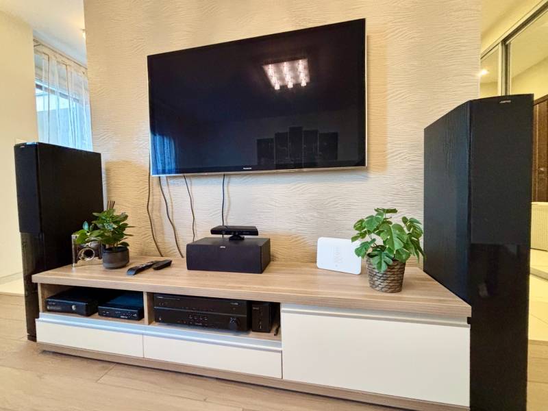 Televízió a nappali falán dekoratív növényekkel és elektronikával a szekrényen.