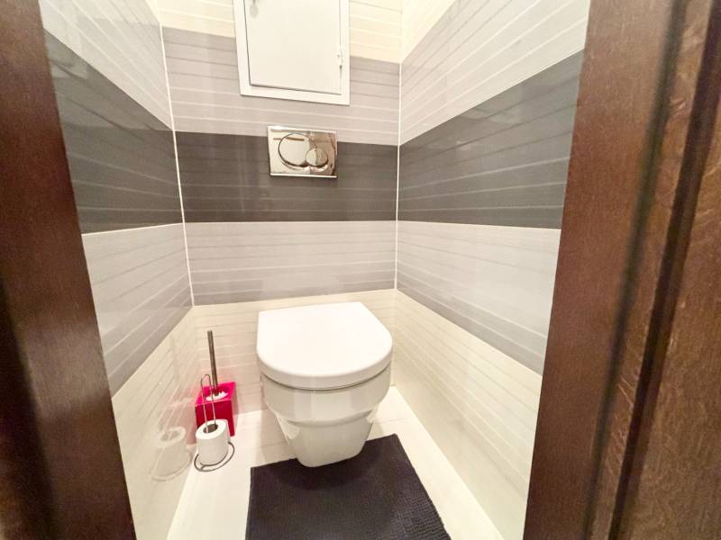 Toalett egy kétszobás lakásban fehér és szürke csempékkel a falakon.