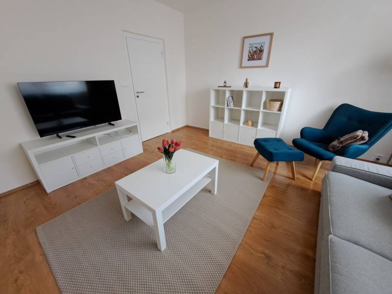 Nappali egy háromszobás lakásban, fa dekoros padlóval és egyszerű bútorokkal.