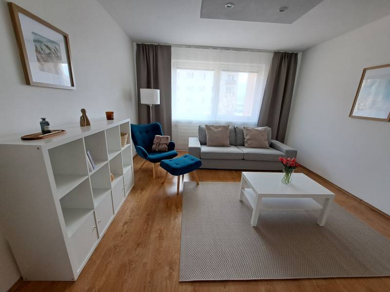 Nappali egy háromszobás lakásban fa dekoros padlóval, kék fotellel és fehér bútorokkal.