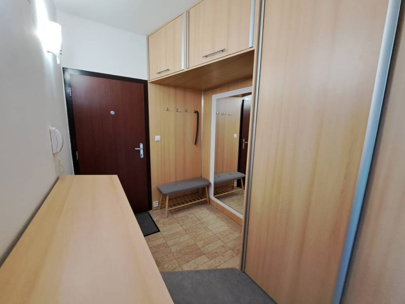 Előszoba egy háromszobás lakásban fogasokkal, tükörrel és szekrények fa dekorációjával.