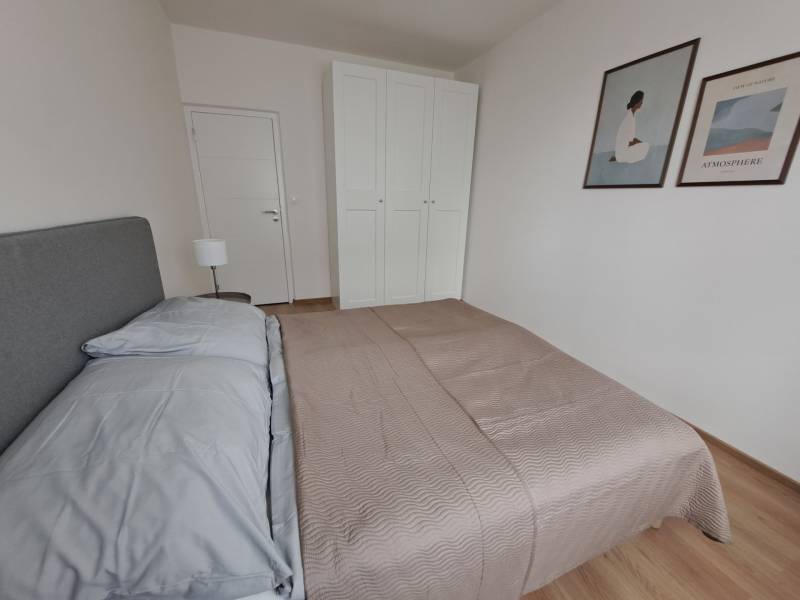 Hálószoba egy háromszobás lakásban ággyal, szekrénnyel és fa dekorú padlóval.