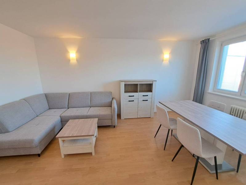 Nappali egy négy szobás lakásban sarokkanapéval és étkezőasztallal.