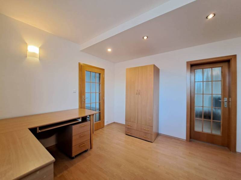 Szoba egy négy szobás lakásban fa mintás padlóval, asztallal és szekrénnyel.