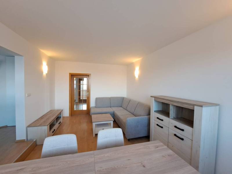 Nappali egy négy szobás lakásban fa mintázatú padlóval és szürke kanapéval.