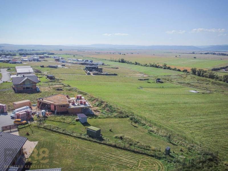 Telkek - lakóhely Mlynicában; épülő házak és kiterjedt mezők a napos égbolt alatt.