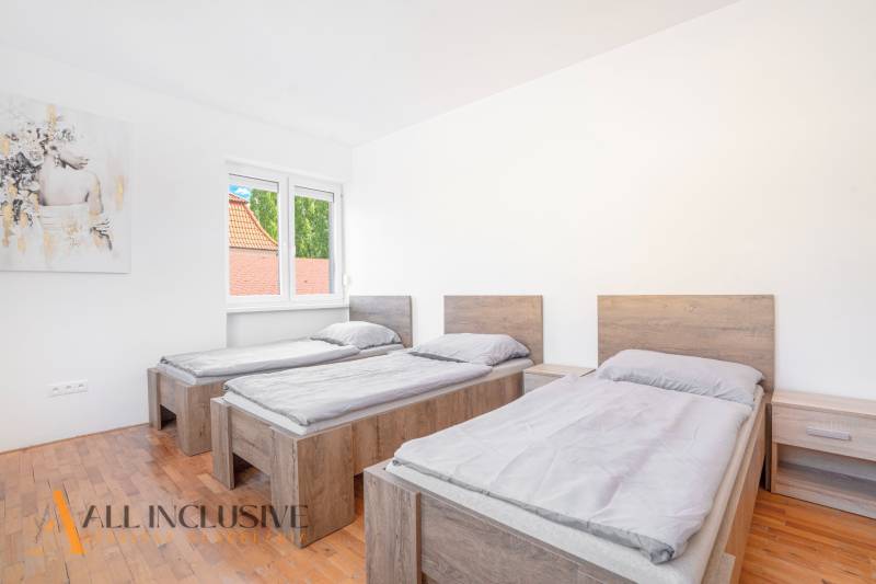 Három ágy a szobában fa mintázatú padlóval és egy képpel a falon.