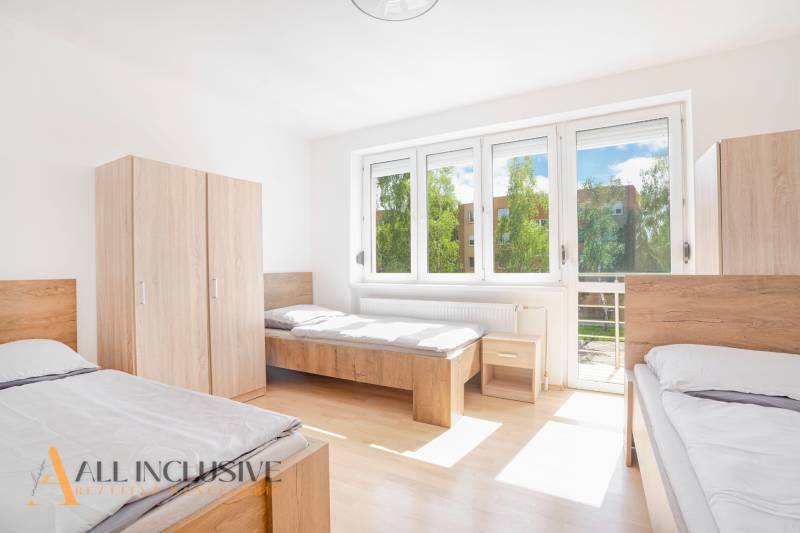 Világos szoba három ággyal, fehér falakkal, szekrényekkel és nagy ablakokkal.