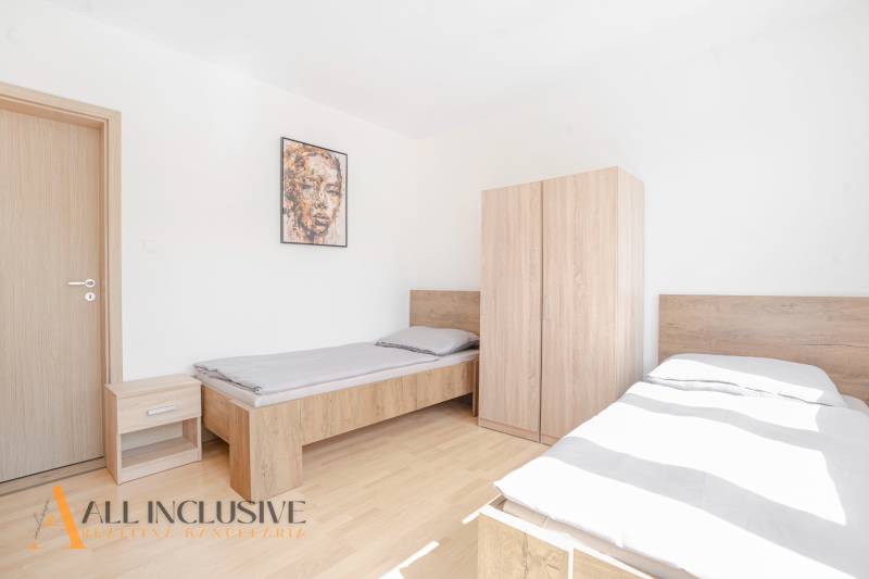 Hálószoba két ággyal és bútorokkal, fa mintázatú padló, kép a falon.