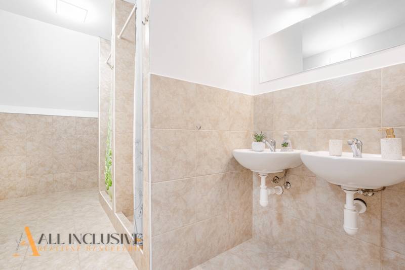 Két mosdókagylós és zuhanyzós fürdőszoba, dekoratív csempék és tükör az épületben.