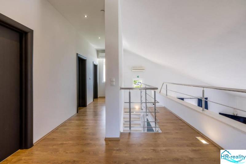 A villa belső tere fehér falakkal, fa dekorációjú padlóval és korláttal.