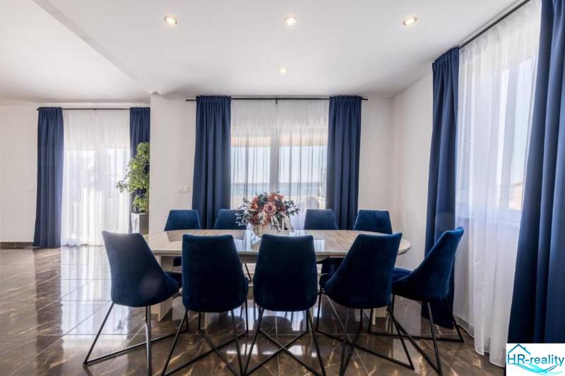 Ebédlő a villában sötét függönyökkel, fa mintázatú padlóval és kék székekkel.