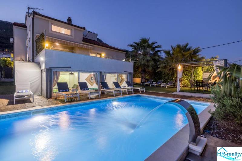 Villa Kaštelában megvilágított medencével, napozóágyakkal és pálmafákkal a kertben alkonyatkor.