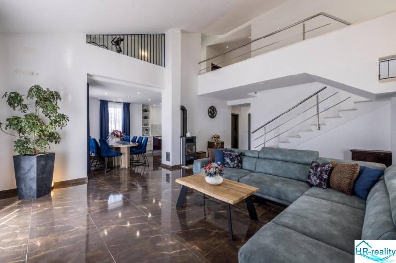 Nappali egy villában kényelmes kanapéval, étkezővel és lépcsővel, fa dekorációjú padlóval.