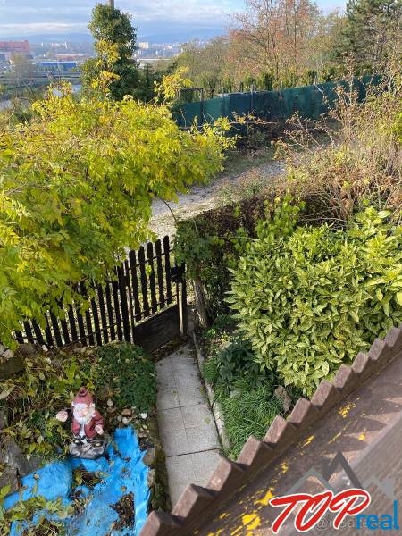 Kert a ház mellett Felsővályban, sétánnyal, zöldterülettel és kerti dekorációval.