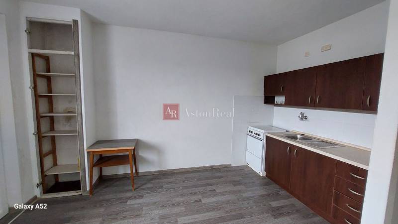 Konyha egy egyszobás lakásban sötét szekrényekkel és fa dekorációjú padlóval.