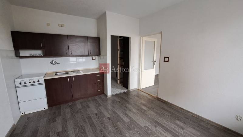 Konyha sötét szekrényekkel és fa dekorációjú padlóval egy egyszobás lakásban.