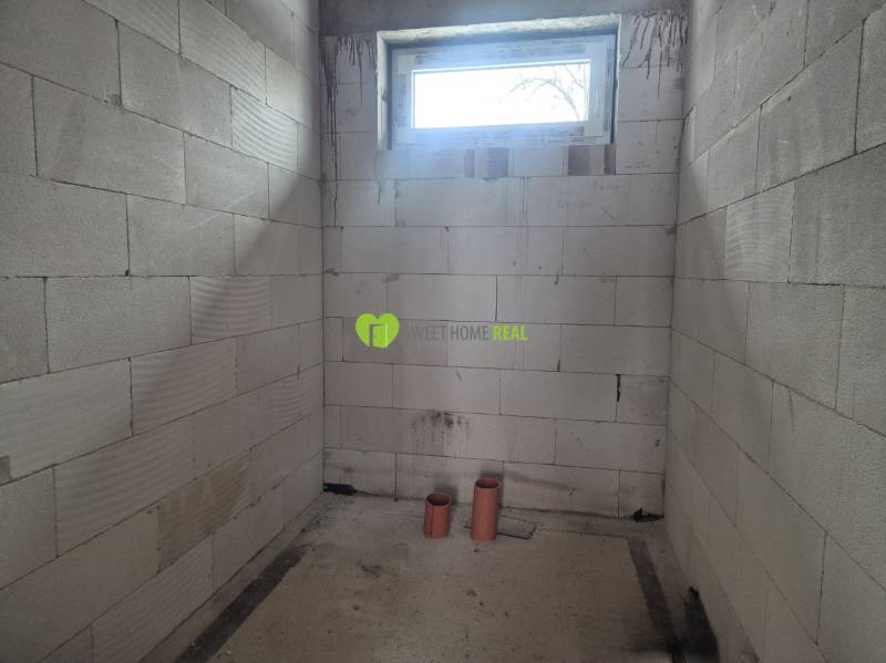 Vakolatlan falak, kis ablak és PVC csövek a családi házban.