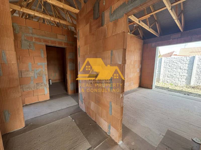 Félkész családi ház vakolatlan falakkal és fa tetőszerkezettel.