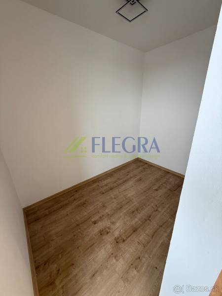 Üres szoba egy egyszobás lakásban, fa mintázatú padlóval, fehér falakkal.