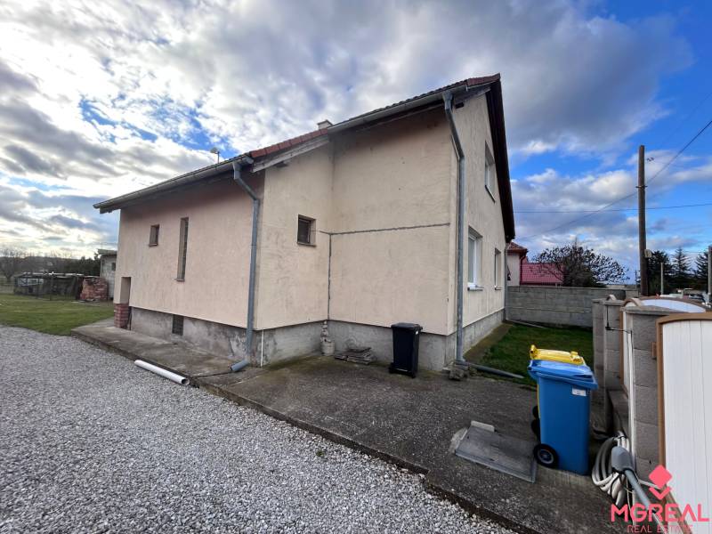 Családi ház Zbehyben mellékúttal, gyepfelülettel és kék szemetes edénnyel.