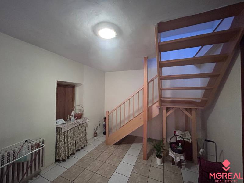 Családi ház belső tere fa lépcsővel, asztallal és kerámia csempével burkolt padlóval.