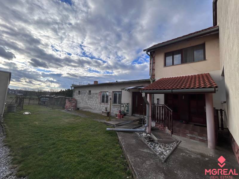 Családi ház Zbehyben gyepes udvarral, kerttel és kövezett sétánnyal a felhős ég alatt.