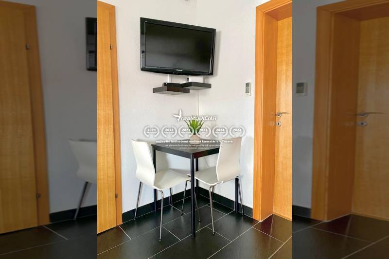 Ebédlő egy családi házban sarokasztallal, falra szerelt televízióval és fekete csempékkel.