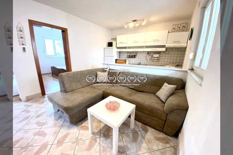 Családi ház belső tere kanapéval, fehér asztallal és konyhasarokkal.