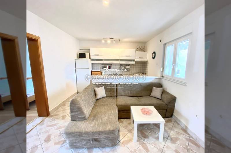 Nappali családi házban kanapéval és konyhasarokkal, padlón csempe.