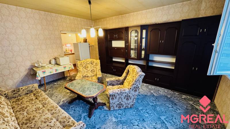 Nappali egy kétszobás lakásban régebbi bútorokkal és szőnyeggel a padlón.