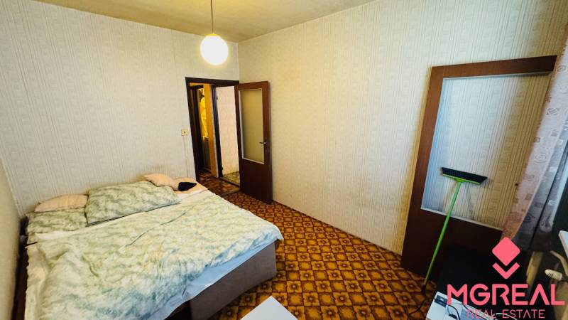 Hálószoba szőnyeggel, ággyal és világos falakkal egy kétszobás lakásban.