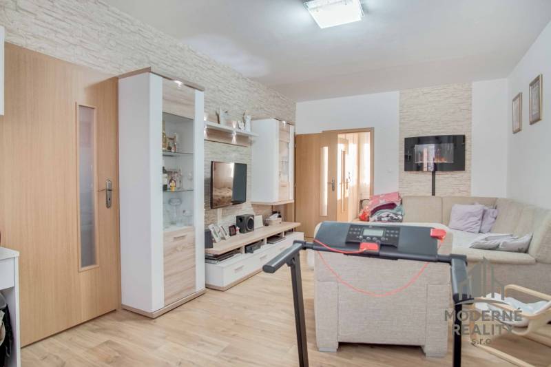 Nappali egy háromszobás lakásban, fa dekoros padlóval és sarokkanapéval.