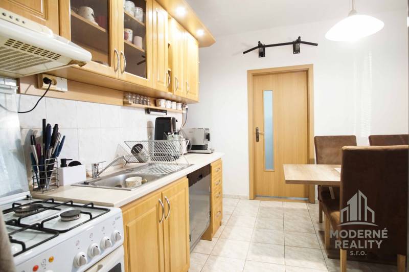 Konyha egy háromszobás lakásban fa szekrényekkel és étkezőasztallal.