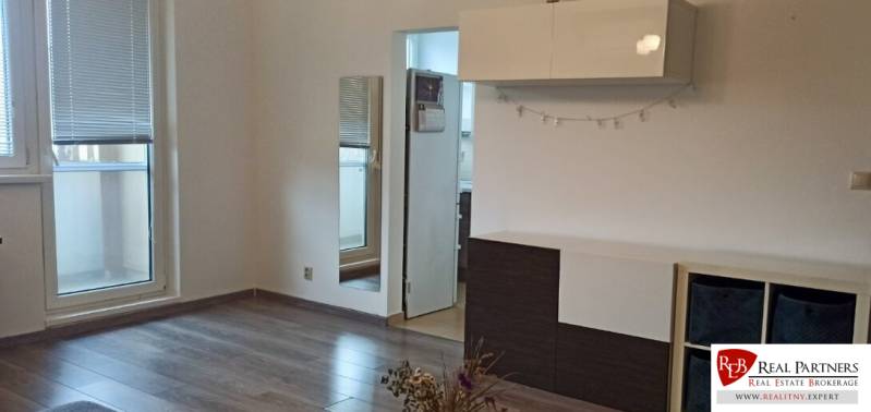 Nappali egy kétszobás lakásban, fa dekoros padlóval, fehér bútorokkal és tükörrel.