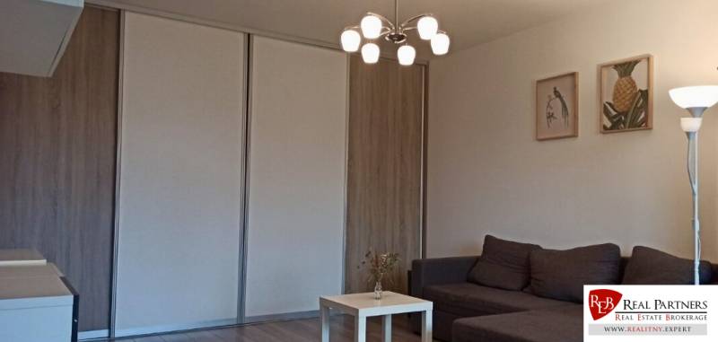 Nappali kanapéval, asztallal és fa dekorációjú padlóval egy kétszobás lakásban.