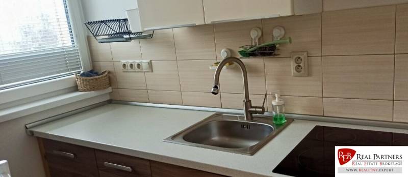 Konyha egy kétszobás lakásban mosogatóval, kerámia főzőlappal és kosárral az ablak mellett.