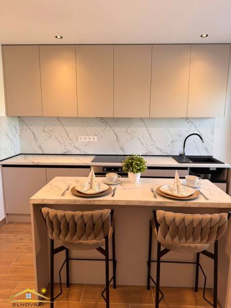 Konyha bárpulttal, fa hatású padlóval és világos bútorokkal egy kétszobás lakásban.