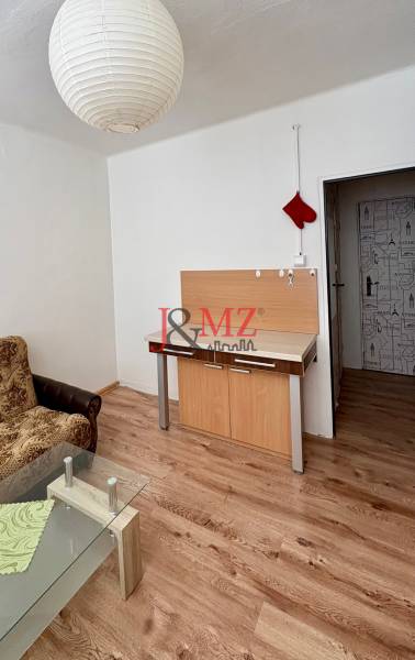 Garzonlakás kanapéval, üvegasztallal és fa mintázatú padlóval.