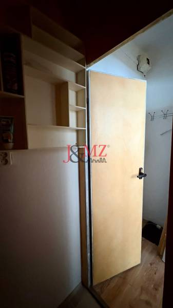 Nyitott ajtó, fal polcokkal, kampók. Garzonlakás fa dekor padlóval.