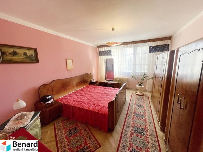 Hálószoba egy háromszobás lakásban piros kiegészítőkkel és fa dekorációjú padlóval.