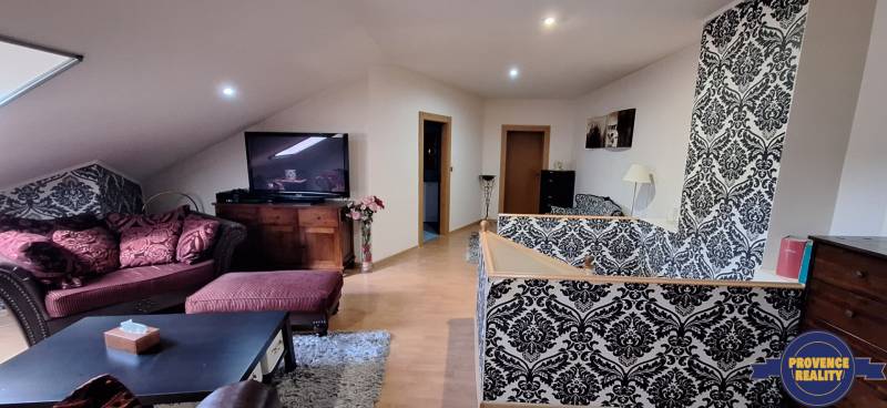 Nappali egy családi házban kanapéval, mintás tapétával és TV-vel.