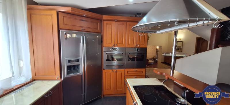 Konyha egy családi házban fa szekrényekkel és rozsdamentes acél készülékekkel.