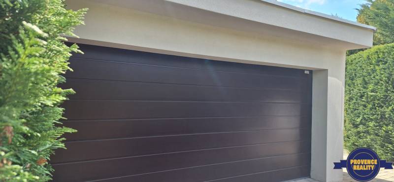 Családi ház garázsajtaja Komáromban, zölddel körülvéve.