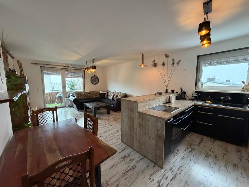 Nappali konyhával egy háromszobás lakásban, fa mintázatú padlóval.