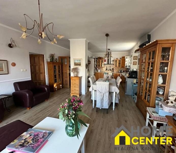 Nappali konyhával családi házban, fa dekoros padló, virágok az asztalon.