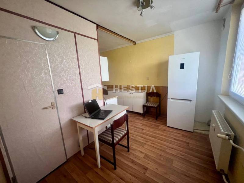 Konyha egy háromszobás lakásban, íróasztallal, hűtőszekrénnyel és fa padlóval.