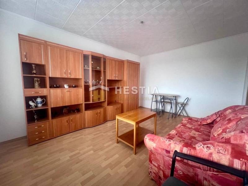 Nappali egy háromszobás lakásban piros kanapéval és fa nappali szekrénnyel.