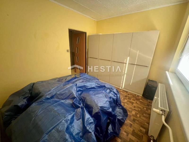 Szoba szekrénnyel, radiátorral és letakart bútorral egy háromszobás lakásban.